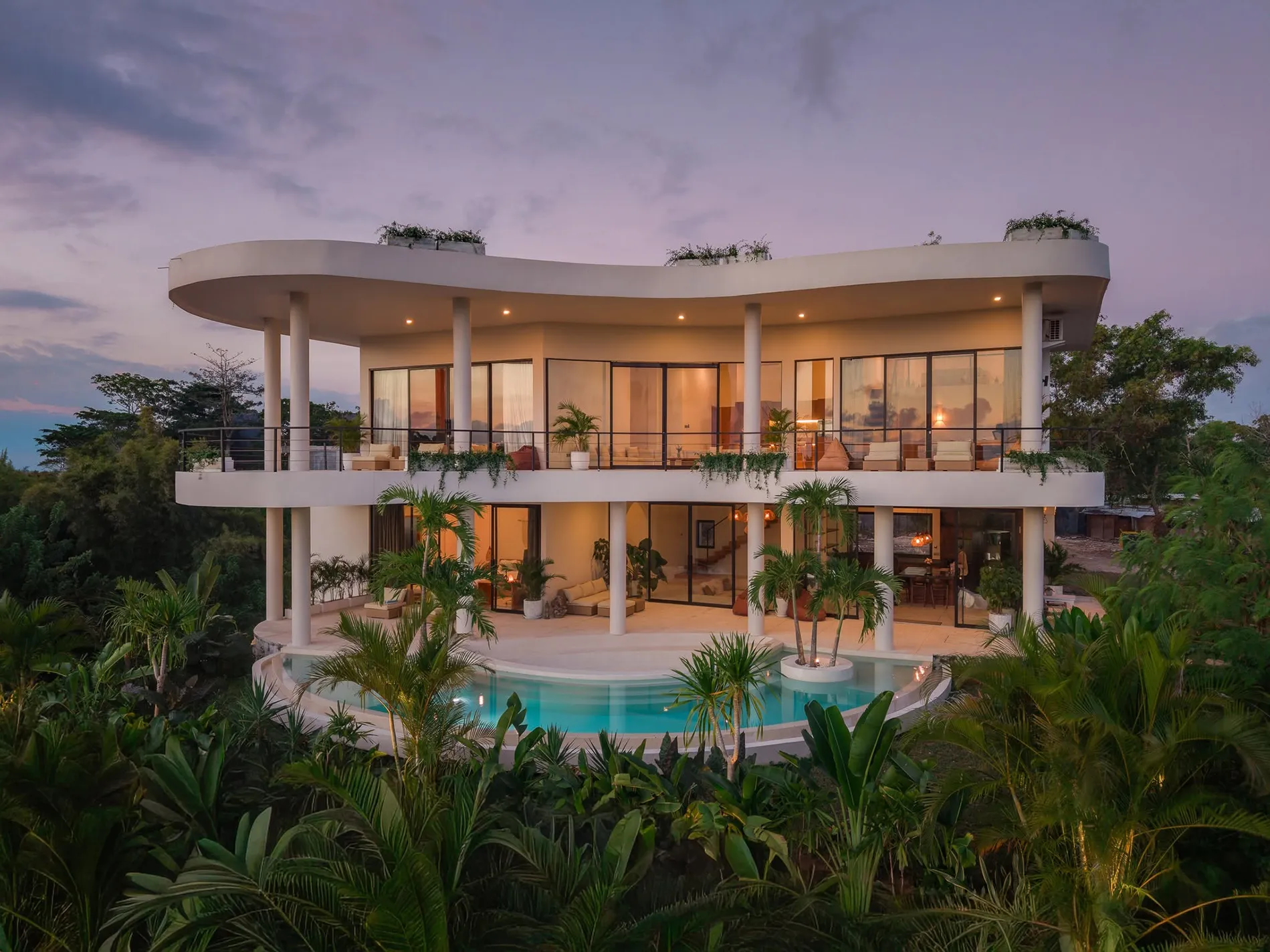 Curved white villa glowing at dusk above a rounded pool at The Sanctuary Retreat Centre